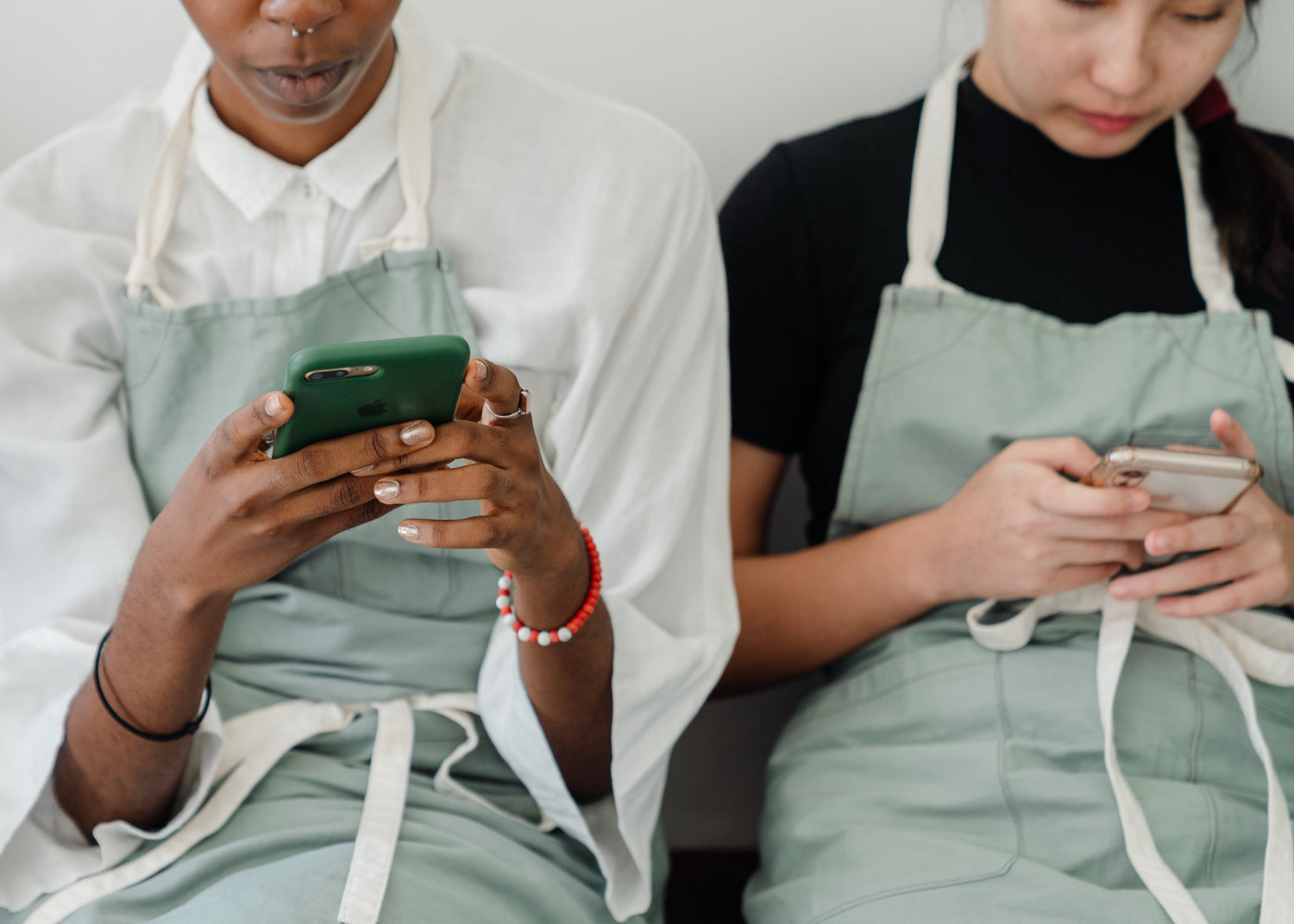 Two people in aprons, sitting and using their smartphones.