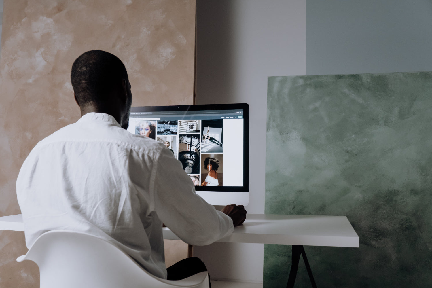 Man in a white shirt viewing photos on a large computer screen at a desk.