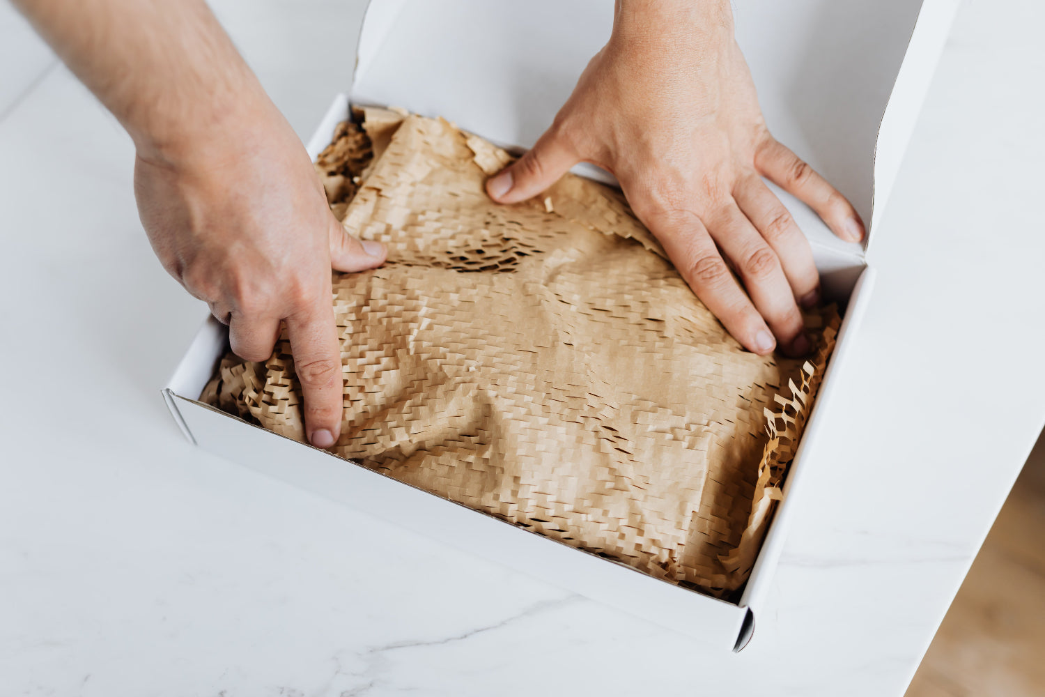 Hands unwrapping a package with brown paper packaging material.