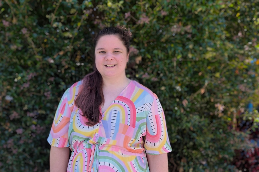 Nataasha Torzsa stands in front of a garden wearing a rainbow dress