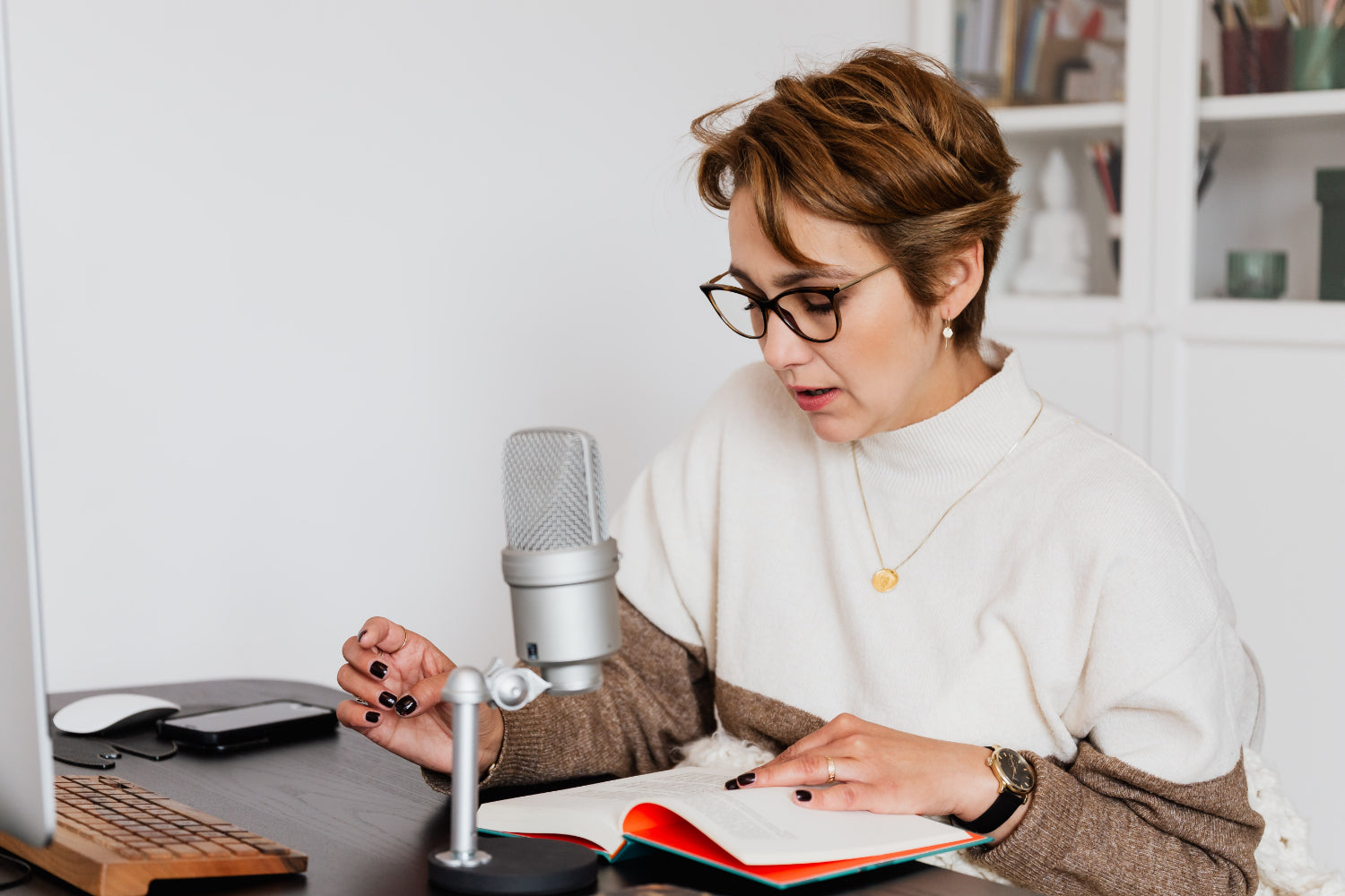 Woman reading a book into a microphone while sitting at a desk