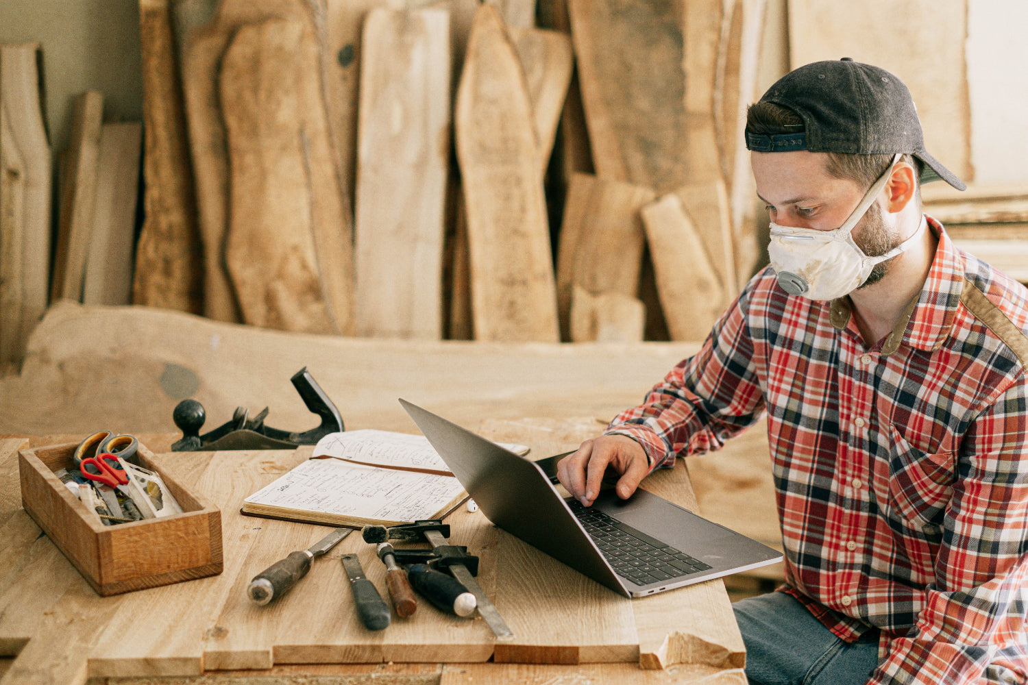 Woodworker wearing a mask, working on a laptop in a workshop